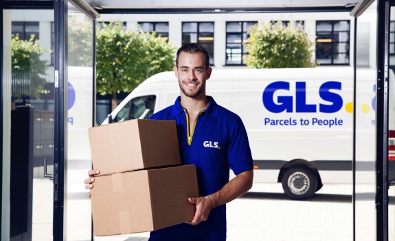 Een bezorger staat met een pakket voor zijn camionnette