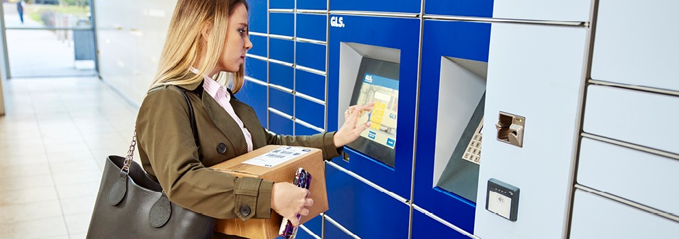 Femme récupérant un colis dans un casier automatique GLS, utilisant l’écran tactile pour entrer ses informations.